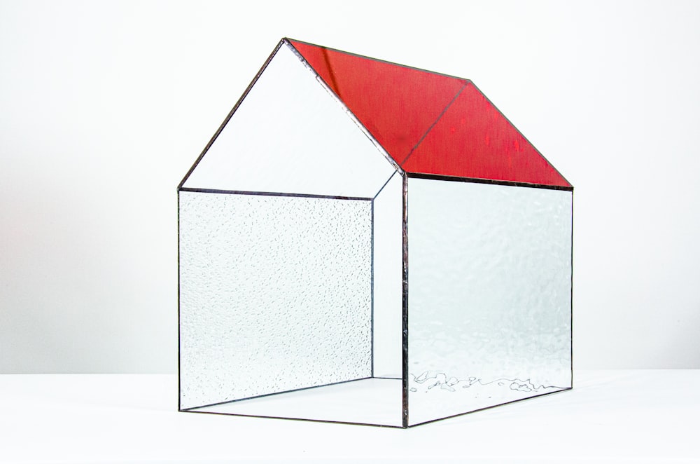a glass house with a red roof on a white surface