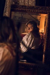 A sensual and elegant woman smiling softly in a dimly lit room, embodying mystery and allure.