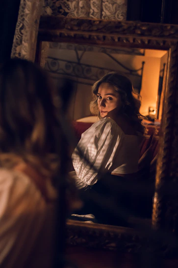 A sensual and elegant woman smiling softly in a dimly lit room, embodying mystery and allure.