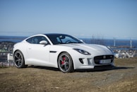 A pristine white sports coupé parked on a coastal cliff overlooking the ocean.