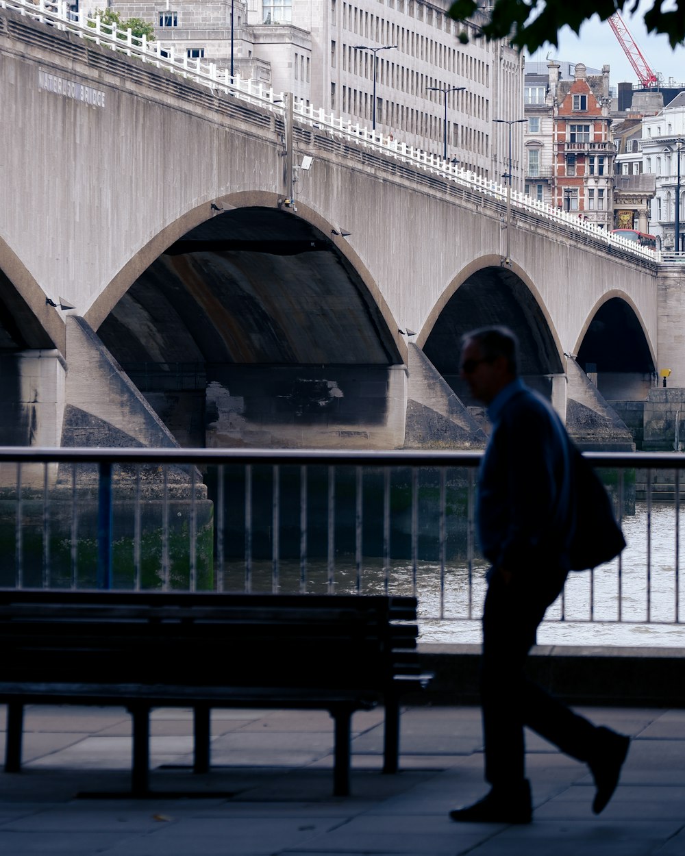 a man walking down a sidewalk next to a bridge