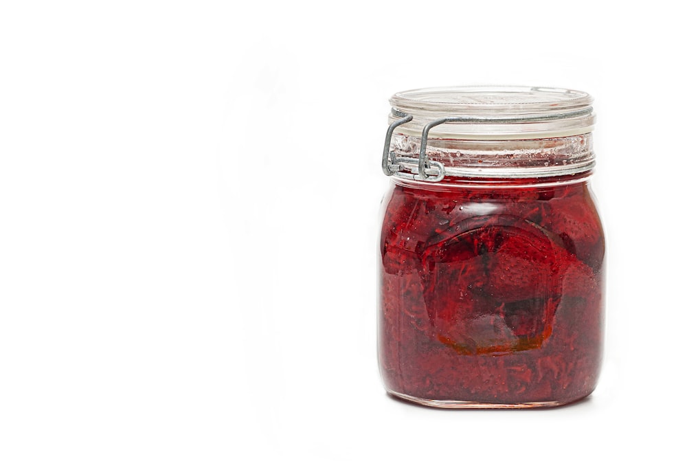 a glass jar filled with red liquid on a white background