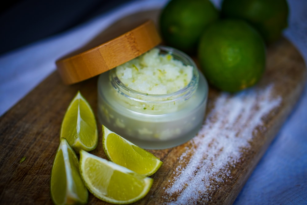 a wooden cutting board topped with limes and a jar of cream