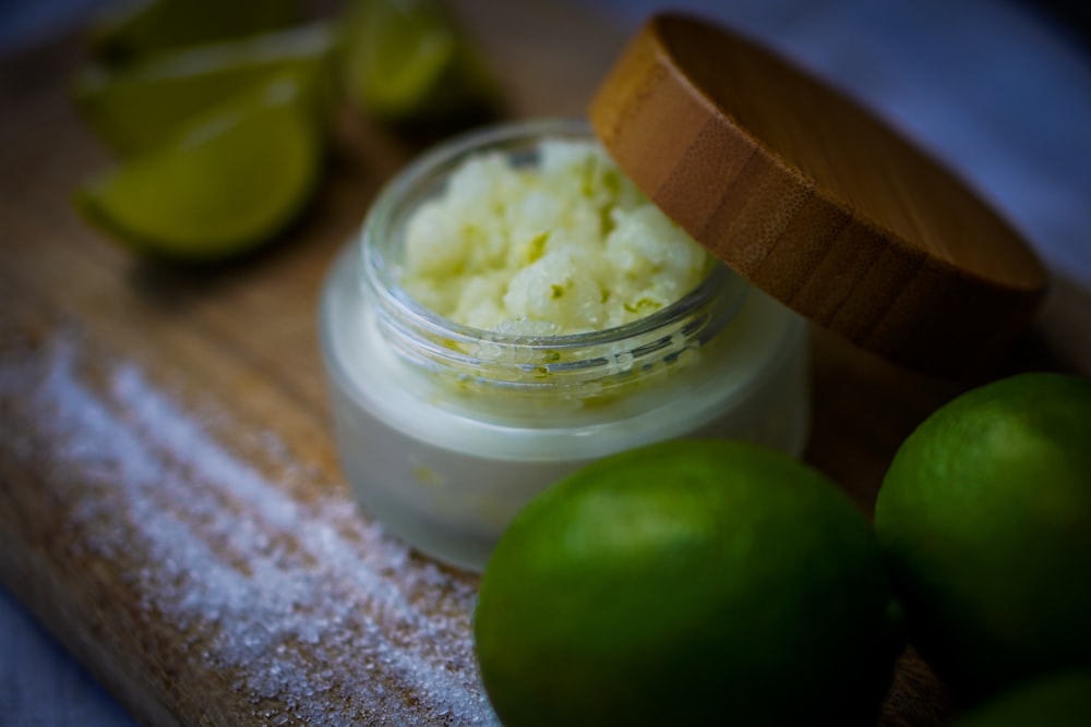 a close up of a jar of cream next to limes