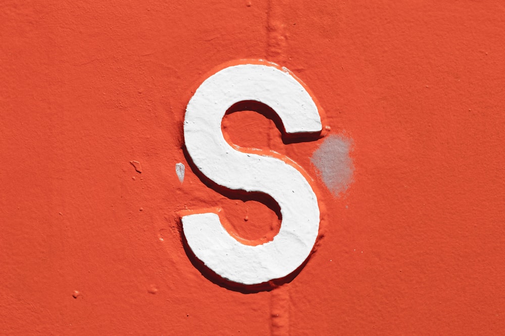 Un primer plano de una letra blanca S en una pared naranja