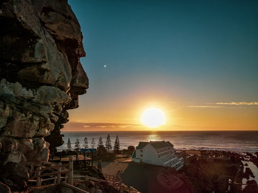 the sun is setting over a rocky cliff by the ocean