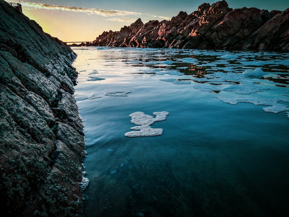 a body of water with rocks and a bridge in the background