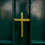 A gold cross is prominently displayed on a dark green, textured background, likely a door or a wall.