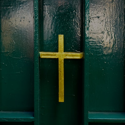 A gold cross is prominently displayed on a dark green, textured background, likely a door or a wall.