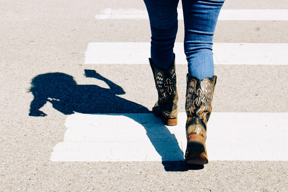a woman walking across a cross walk wearing cowboy boots