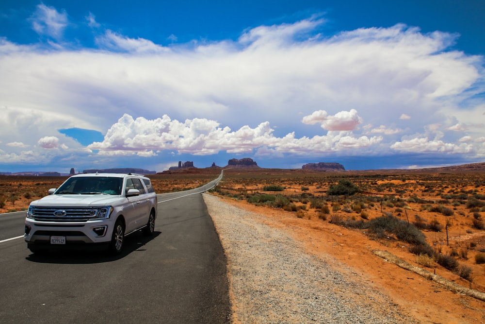 a white suv driving down a desert road