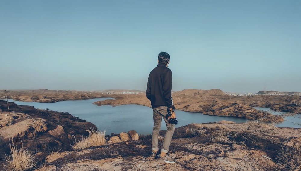 a man standing on top of a rocky hill next to a lake