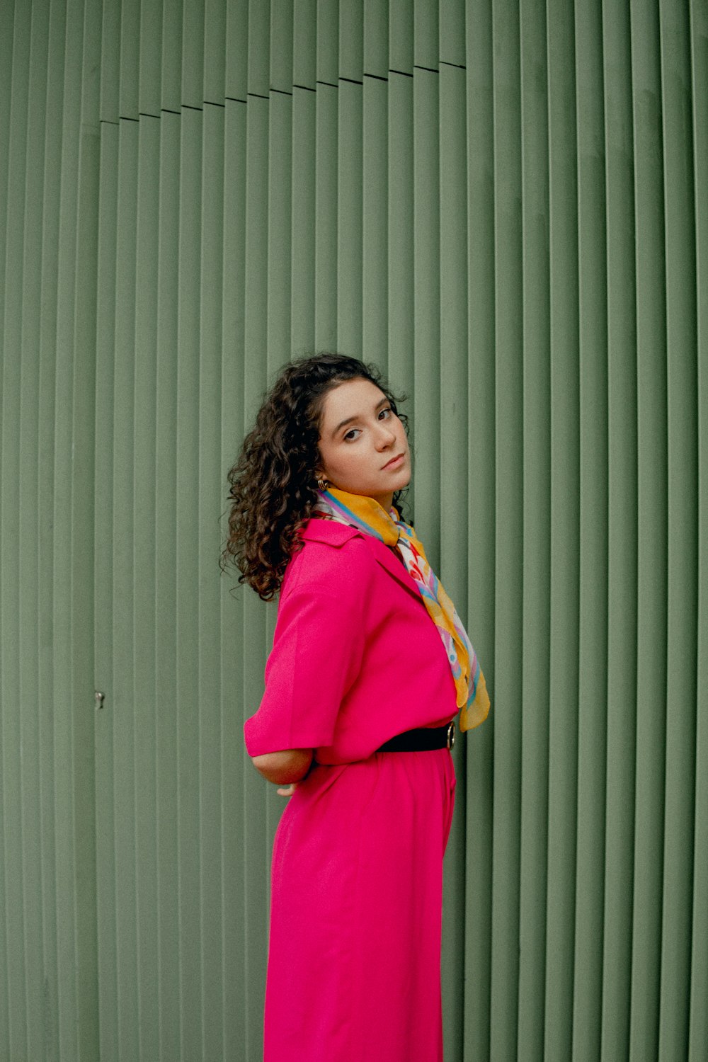 uma mulher em um casaco rosa está de pé contra uma parede verde
