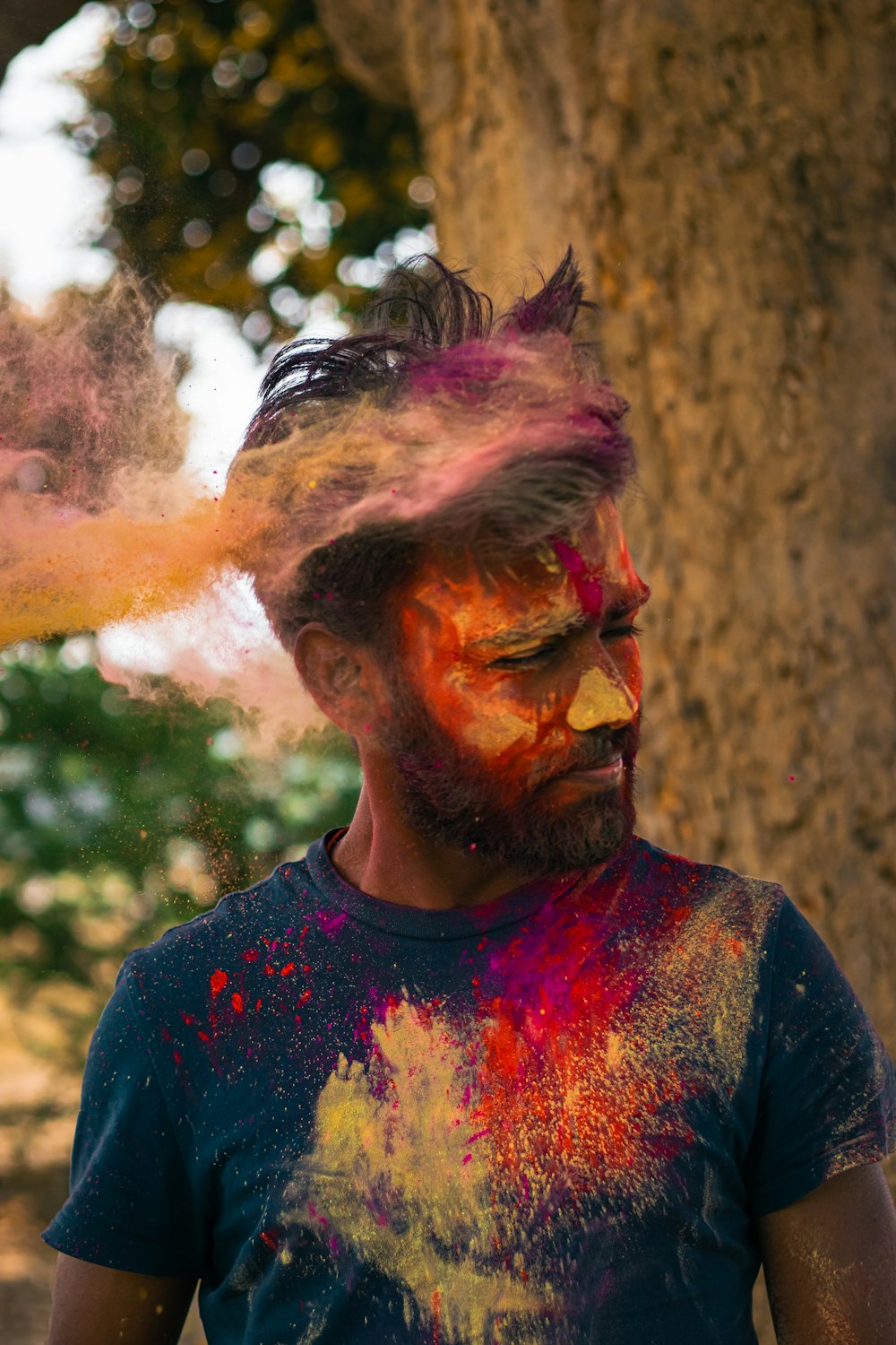 a man covered in colored powder with trees in the background