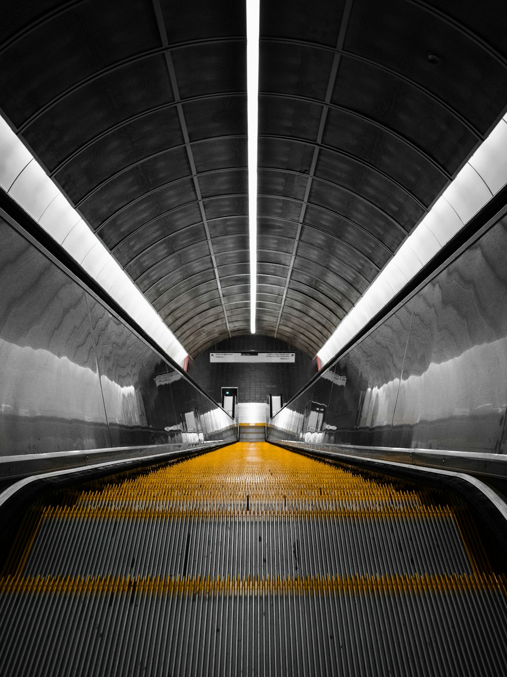 an escalator in a subway station with yellow lines