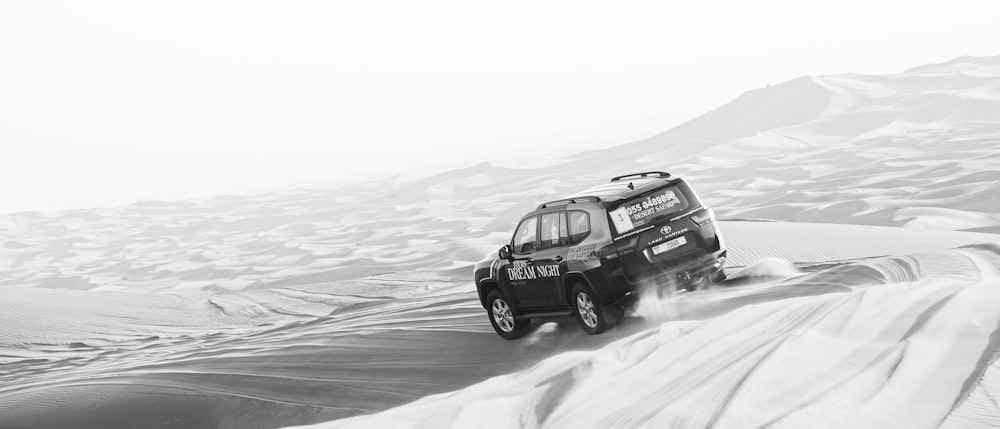 a black and white photo of a vehicle driving through the desert