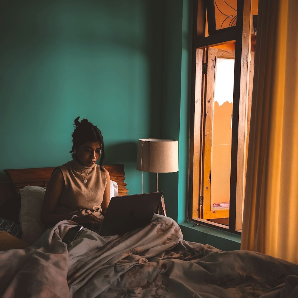 a woman sitting on a bed using a laptop computer