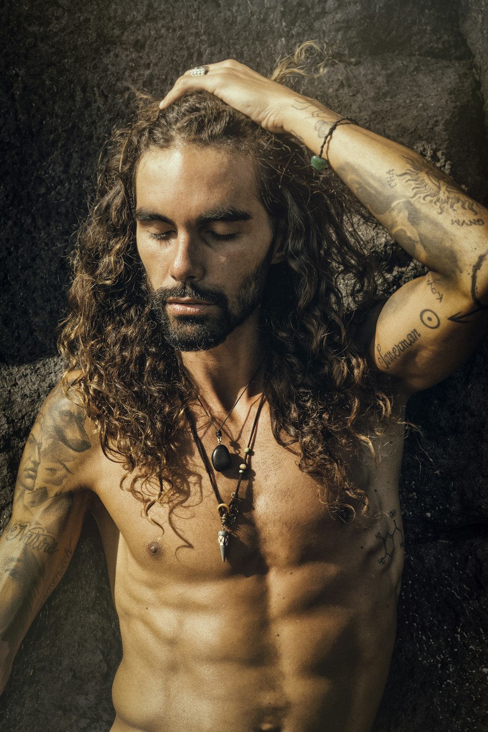 a shirtless man with long hair and tattoos