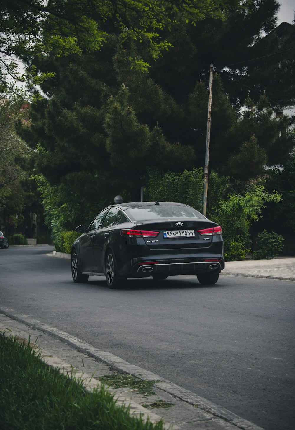 a black car driving down a street next to a forest