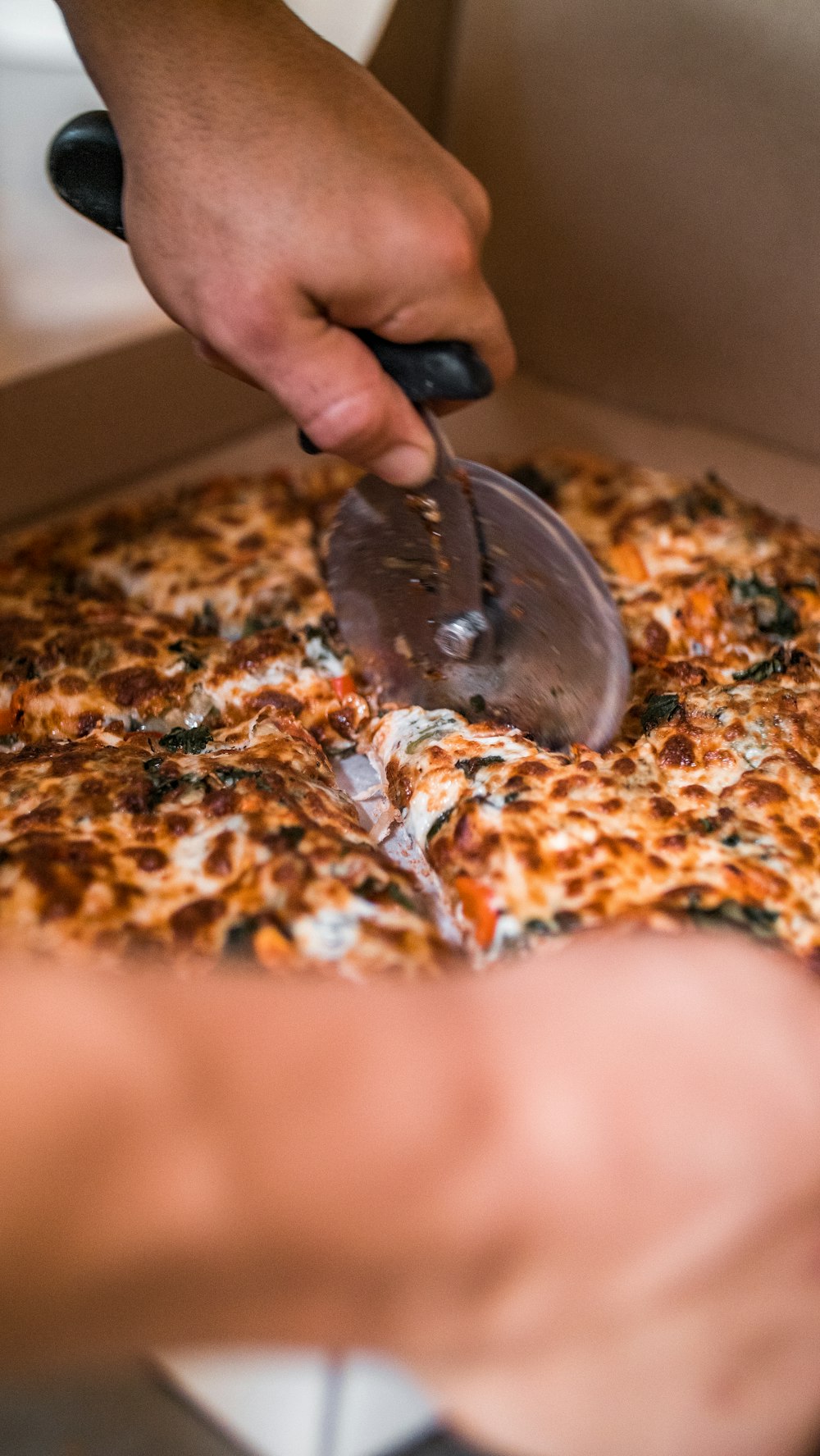 a person cutting a pizza with a pizza cutter