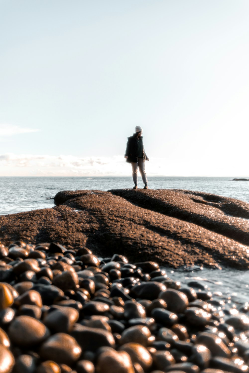 a man standing on top of a rocky beach next to the ocean