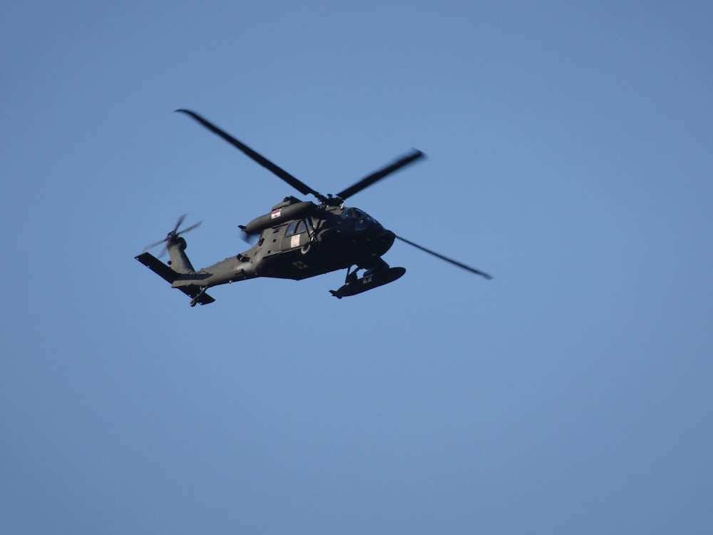 a military helicopter flying through a blue sky