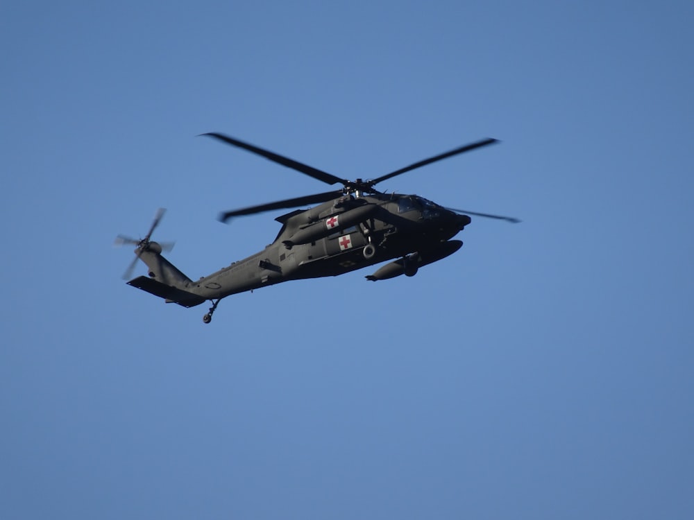 a military helicopter flying through a blue sky