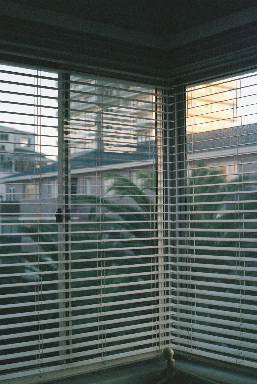 a window with blinds in a room with a view of a city