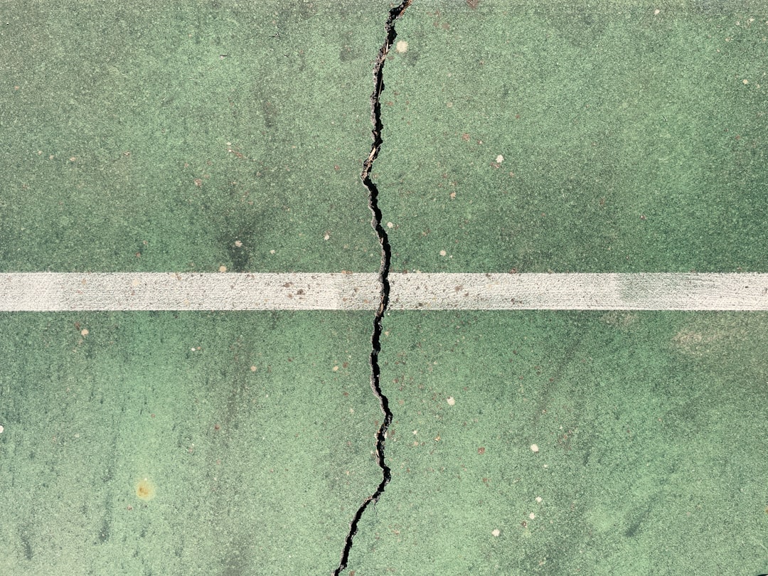 a crack in the ground with a white line going through it, crack on green tennis court