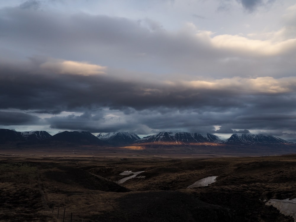 a field with mountains in the distance under a cloudy sky