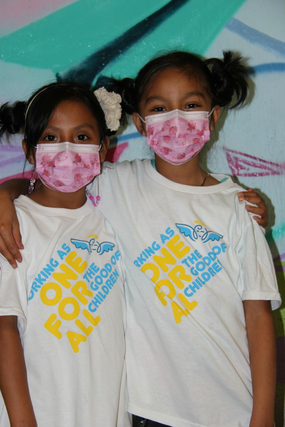 two young girls wearing face masks in front of a graffiti wall