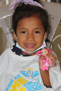 A joyful child holding a handmade doll wearing a tiny 'Jesus is Enough' t-shirt