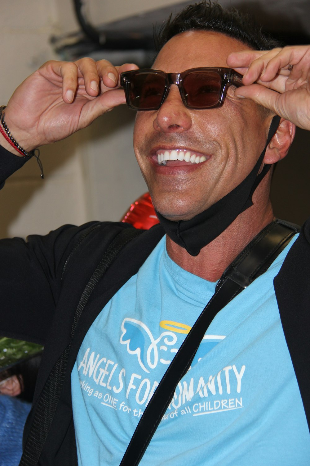 a man in a blue shirt is holding up his sunglasses