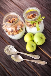 two jars of yogurt and apples on a wooden table