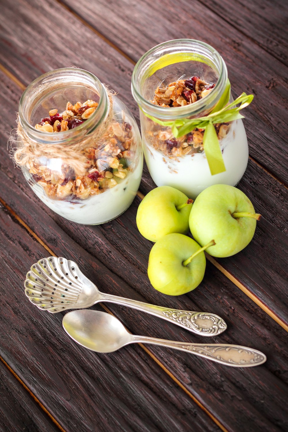 two jars of yogurt and apples on a wooden table