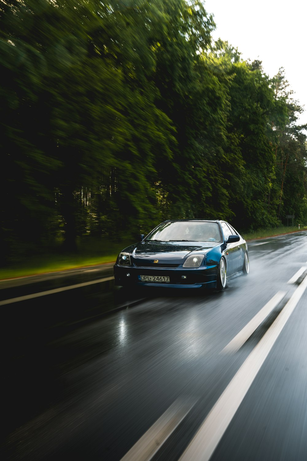 a blue car driving down a wet road