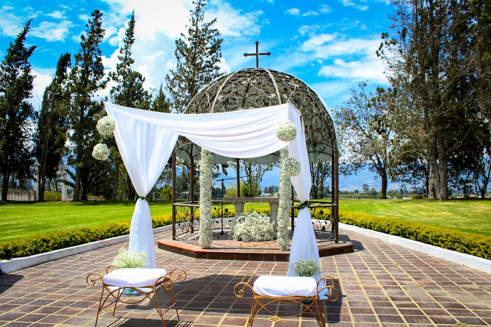 a gazebo with a white drape and chairs