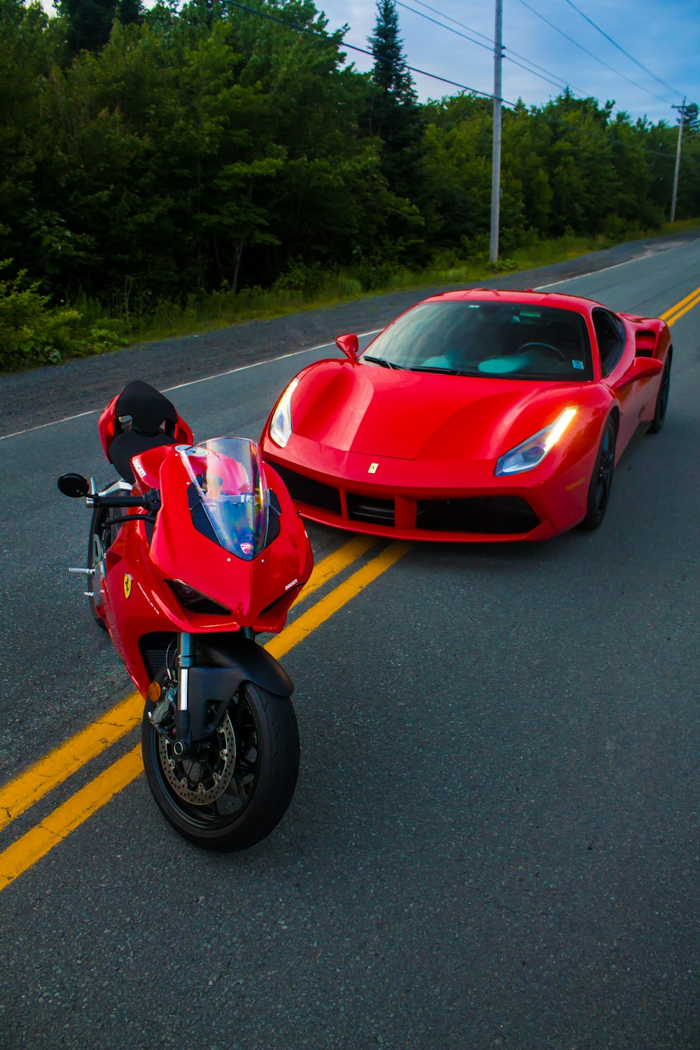 um carro esportivo vermelho e uma motocicleta vermelha em uma estrada