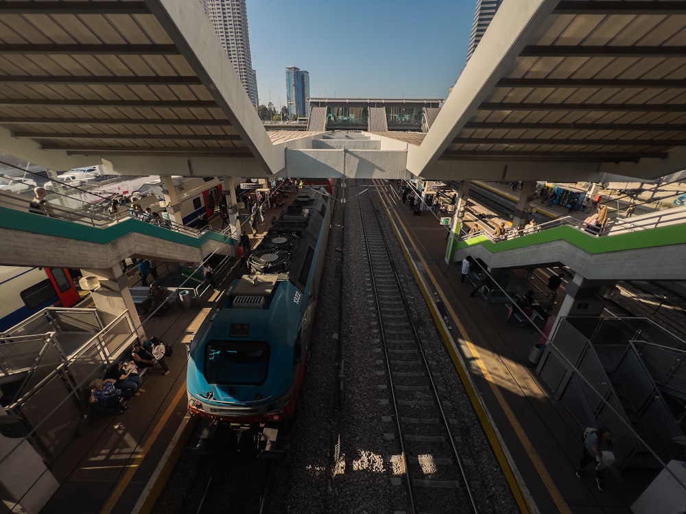 a blue train traveling down train tracks under a bridge