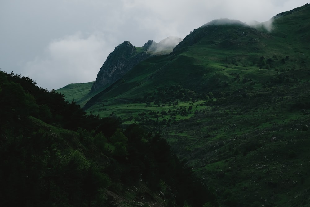 a green mountain with a few clouds in the sky