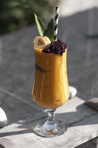 A colorful glass of freshly blended mango shake with a straw on a rustic wooden table.