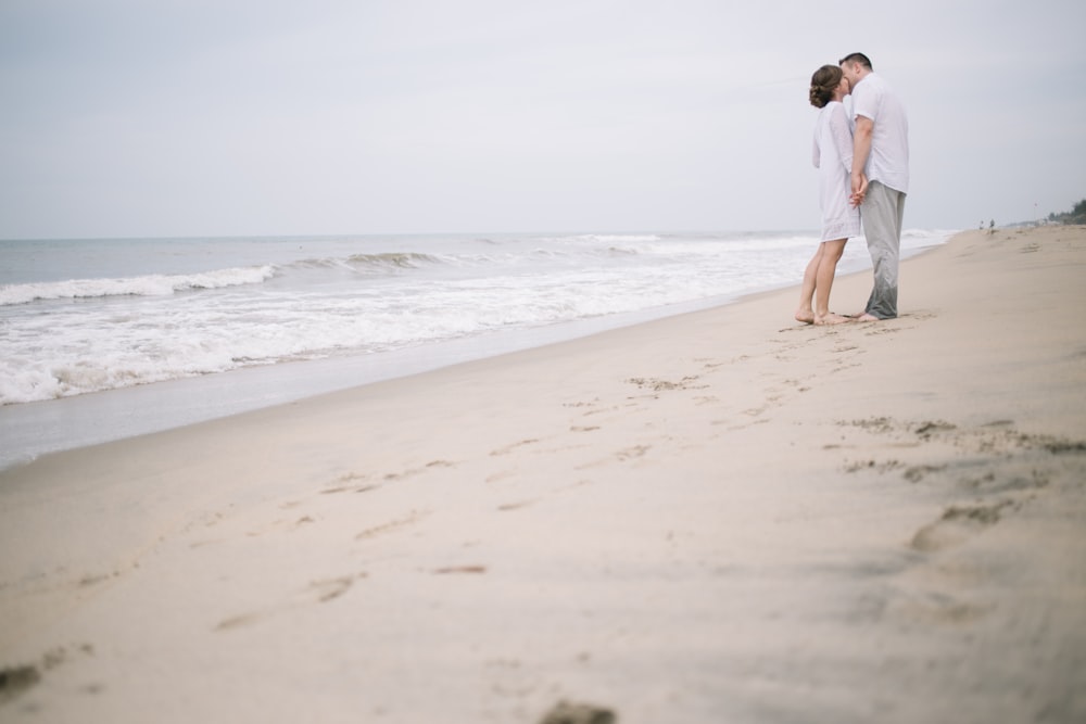 a man and woman standing on a beach next to the ocean