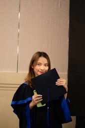 a woman in a graduation gown holding a black piece of paper