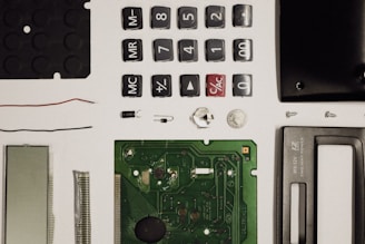 A collection of disassembled electronic components including buttons, a circuit board, a screen, wires, screws, and other small parts, neatly arranged on a white surface.