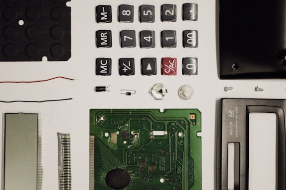 A collection of disassembled electronic components including buttons, a circuit board, a screen, wires, screws, and other small parts, neatly arranged on a white surface.