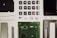 A collection of disassembled electronic components including buttons, a circuit board, a screen, wires, screws, and other small parts, neatly arranged on a white surface.