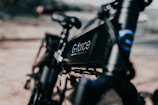 A close-up of a sleek black bicycle with the brand name 'G-force' visible on the frame. The focus is sharp on the bike's frame, while the background is blurred, emphasizing the modern design of the bicycle.