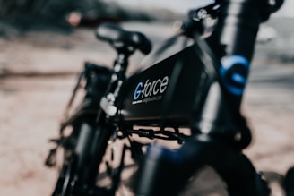 A close-up of a sleek black bicycle with the brand name 'G-force' visible on the frame. The focus is sharp on the bike's frame, while the background is blurred, emphasizing the modern design of the bicycle.