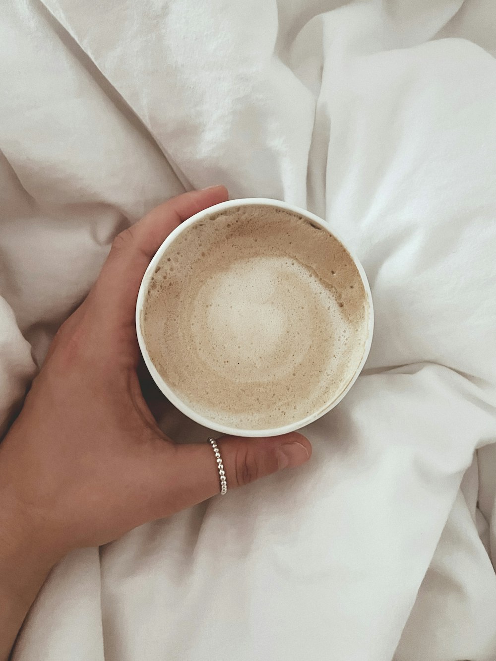 a hand holding a cup of coffee on top of a bed