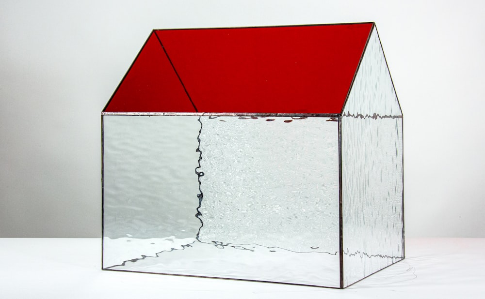 una caja de vidrio con un techo rojo sobre una superficie blanca
